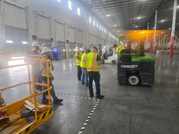 Crew in hi-vis vests observing a forklift operator evaluation inside a Houston warehouse